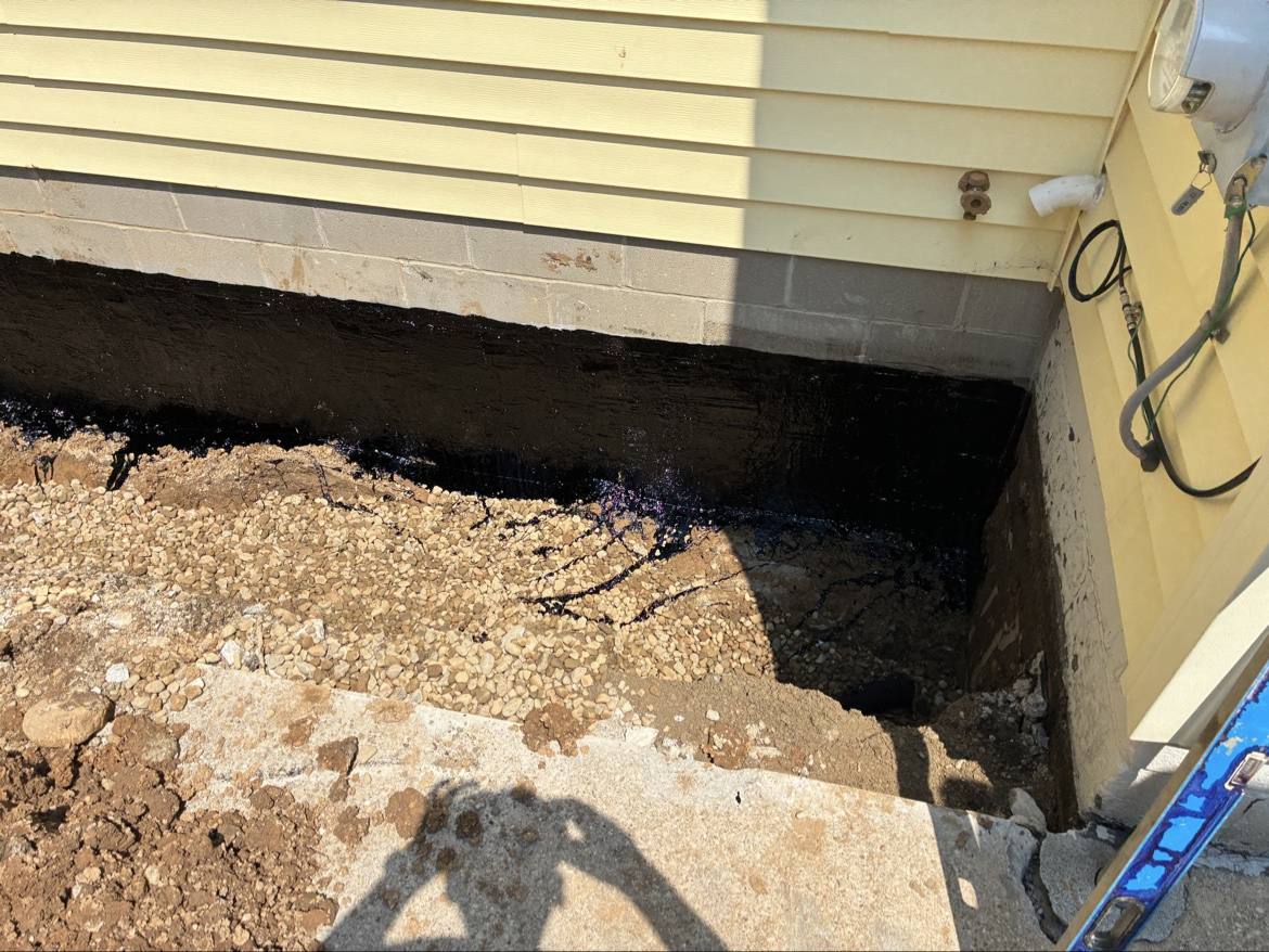 Black waterproofing coating applied to a house foundation wall