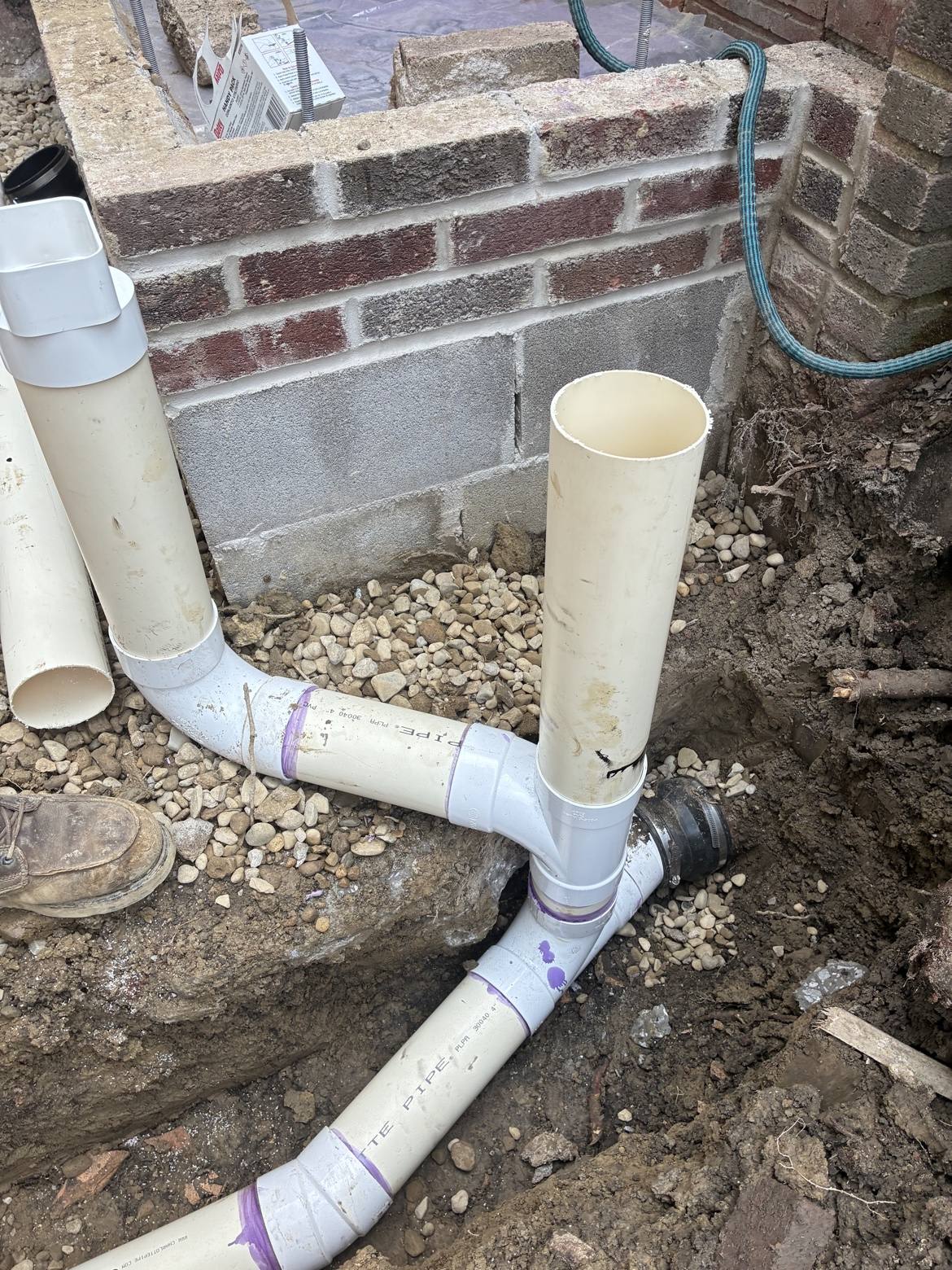 White PVC drainage pipes installed beside a brick foundation