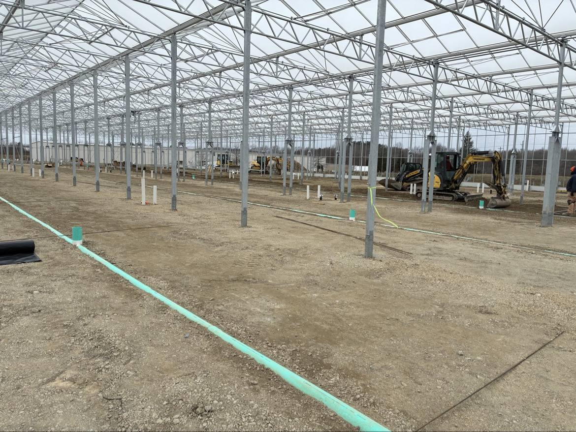 Greenhouse site preparation with excavator and green underground pipe